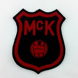 May include: Red and black embroidered patch with the text "MCK" and a soccer ball in the center.