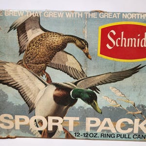 May include: Vintage Schmidt Sport Pack beer box featuring illustrations of ducks in flight. The box has a blue background with the text "THE BREW THAT GREW WITH THE GREAT NORTHWEST" and "SPORT PACK". The box is designed for 12-12 oz. ring pull cans.