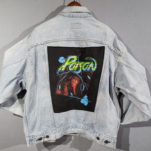 May include: A light blue denim jacket with a black patch on the back. The patch features a graphic of a monster with a red tongue and the word "Poison" in green and blue letters.