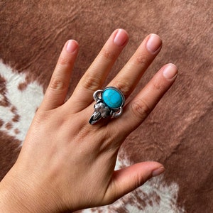 May include: A silver ring with a turquoise stone set in a bull's head design.