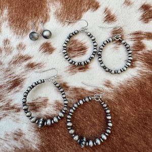May include: A set of silver hoop earrings with a beaded design. The earrings are available in two sizes, with the larger earrings featuring a decorative accent.