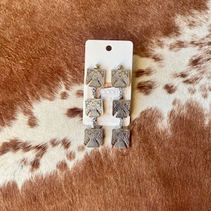May include: A pair of silver dangle earrings with a detailed eagle design. The earrings are on a white card with the text "WOODEN IT BE NICE" and "WESTERN"