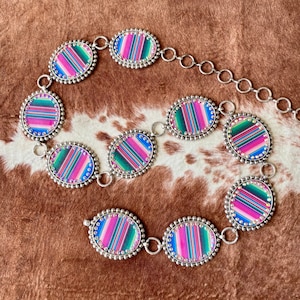 May include: A silver belt with oval-shaped links featuring a colorful striped pattern. Each link is adorned with small rhinestones around the edge.