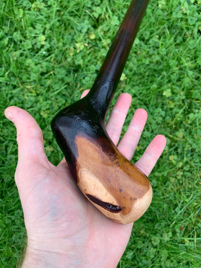 May include: A wooden walking stick with a dark brown finish and a natural wood handle. The handle is shaped to fit comfortably in the hand.