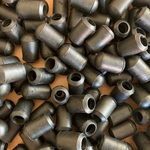 May include: A close-up shot of a pile of black rubber caps. The caps are cylindrical with a rounded top and a hollow opening on one end. They appear to be new and unused, and are scattered in a random pattern.