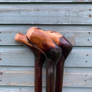 May include: Three wooden walking sticks with dark brown stained wood and natural wood colored tops.