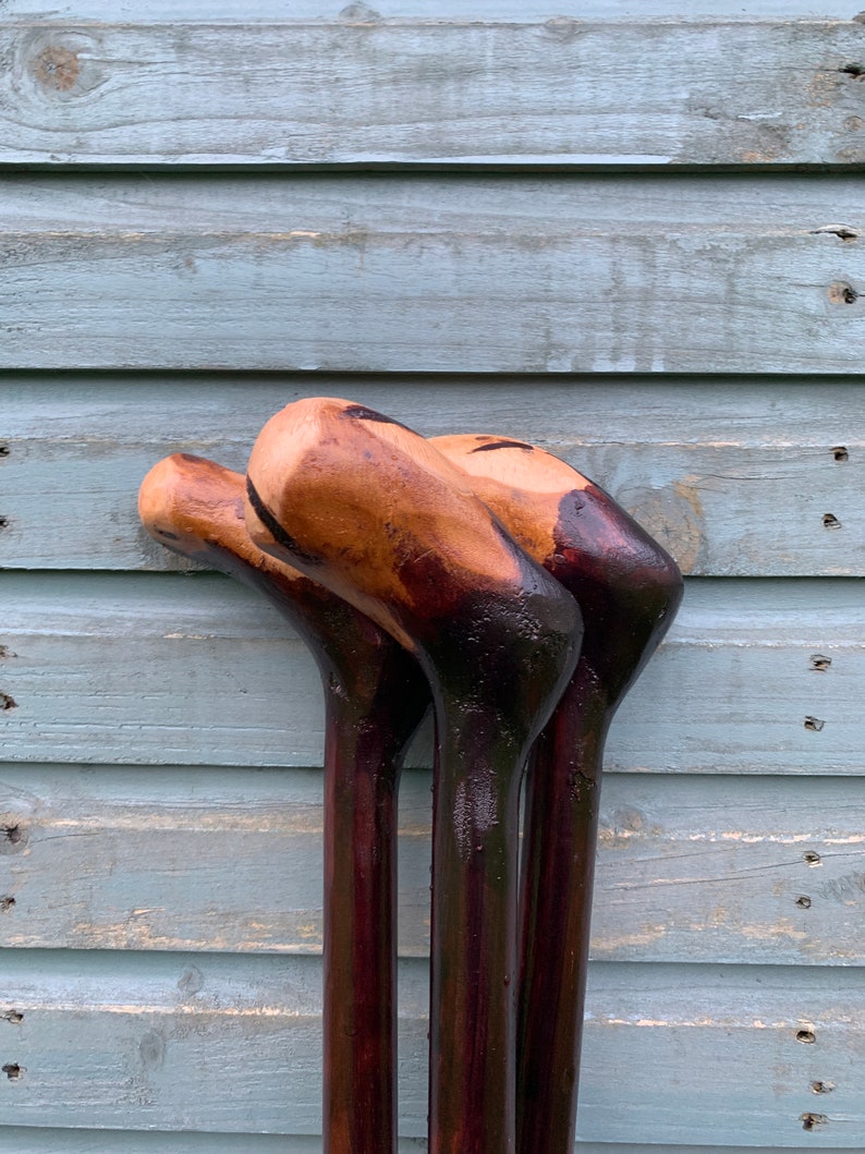 May include: Three wooden walking sticks with dark brown stained wood and natural wood colored tops.