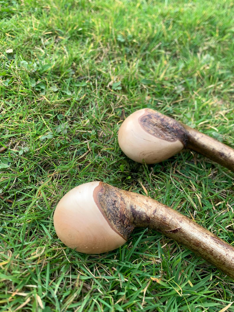 May include: Two wooden walking sticks with smooth, rounded, light brown handles and dark brown bark on the rest of the stick. The sticks are lying on a bed of green grass.