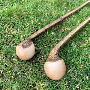 May include: Two wooden walking sticks with a rounded knob at the top. The sticks are brown and have a natural bark finish. The knobs are a light wood color.