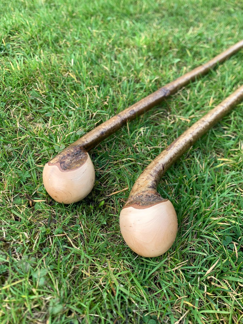May include: Two wooden walking sticks with a rounded knob at the top. The sticks are brown and have a natural bark finish. The knobs are a light wood color.