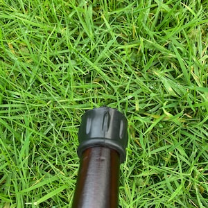 May include: Close-up of a black rubber tip on a brown wooden walking stick.