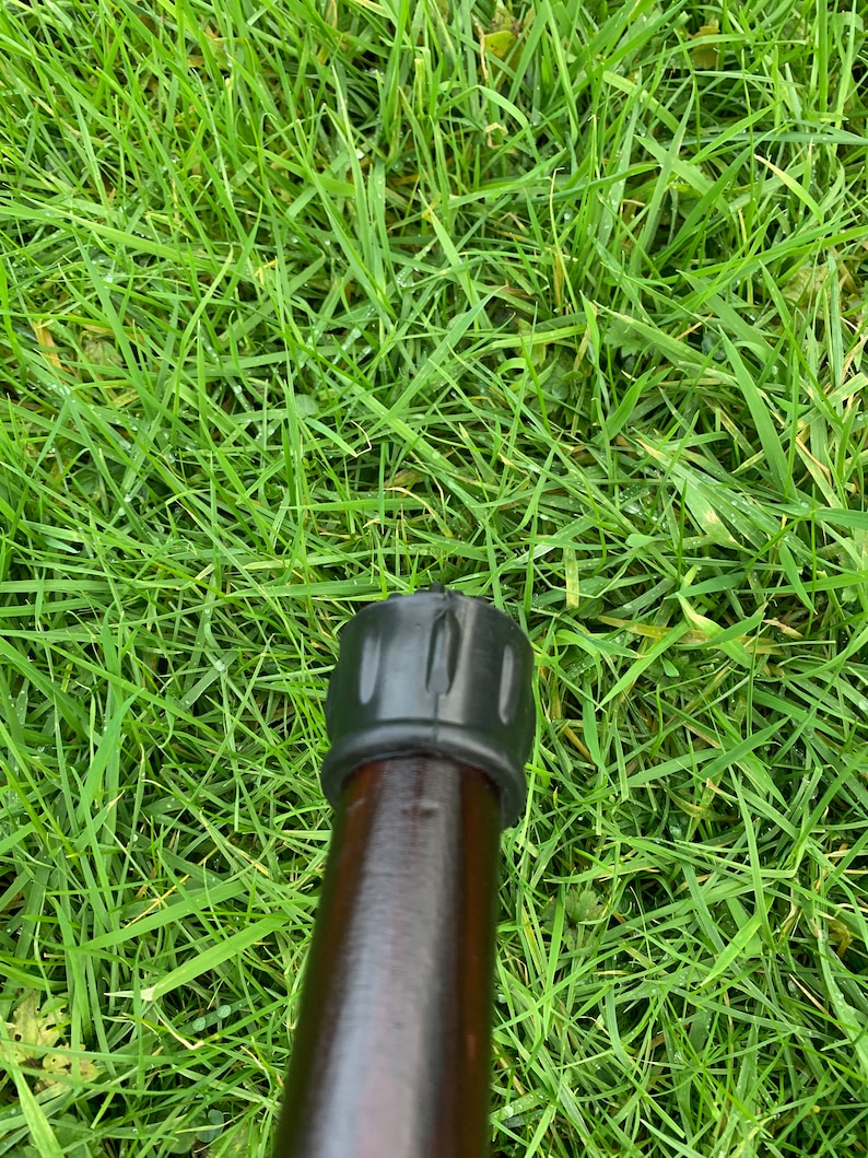May include: Close-up of a black rubber tip on a brown wooden walking stick.