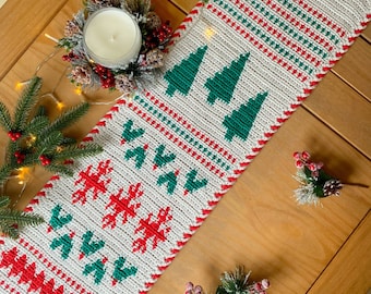 May include: A white crocheted table runner with a red and green Christmas tree design. The runner has a scalloped edge and is decorated with snowflakes and trees.