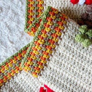 Puede incluir: Primer plano de una manta de ganchillo con un borde multicolor. El borde est&aacute; hecho de hilo verde, naranja, amarillo y marr&oacute;n. La manta est&aacute; hecha de hilo de color crema.