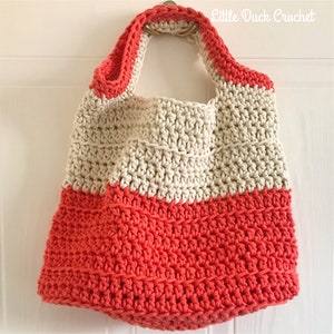 May include: A crocheted tote bag with a cream top and coral bottom. The bag has a single handle and is hanging on a white door.