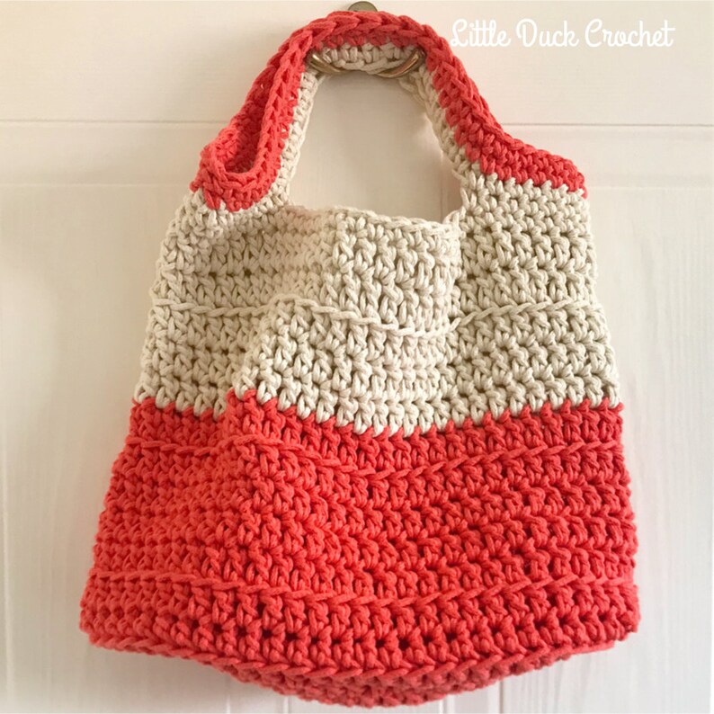 May include: A crocheted tote bag with a cream top and coral bottom. The bag has a single handle and is hanging on a white door.
