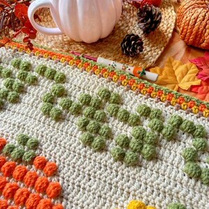Puede incluir: Una manta de ganchillo con un patr&oacute;n texturizado de c&iacute;rculos naranja, amarillo y verde. La manta est&aacute; hecha con hilo beige y tiene un borde de hilo marr&oacute;n, naranja y amarillo.