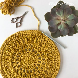Peut inclure: Gros plan sur un dessous de plat rond crochet&eacute; de couleur jaune vif. Le dessous de plat est en cours de r&eacute;alisation avec un crochet et du fil.