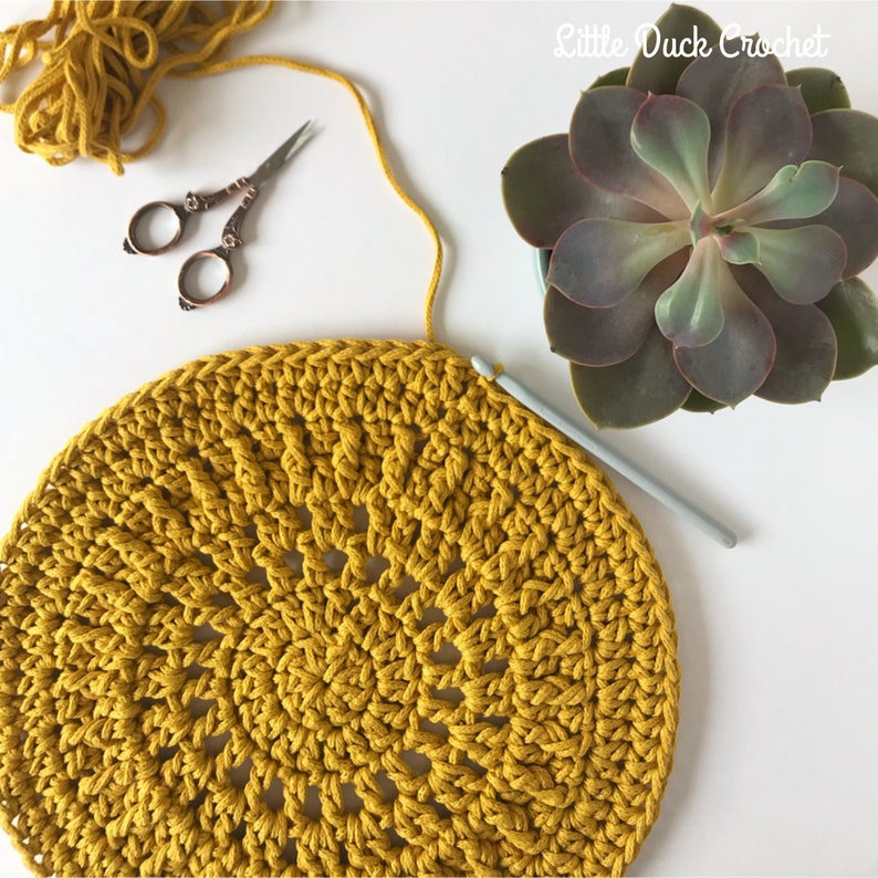 Peut inclure: Gros plan sur un dessous de plat rond crochet&eacute; de couleur jaune vif. Le dessous de plat est en cours de r&eacute;alisation avec un crochet et du fil.