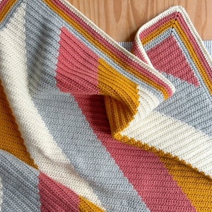 May include: A crocheted baby blanket with stripes of white, gray, pink, and yellow.