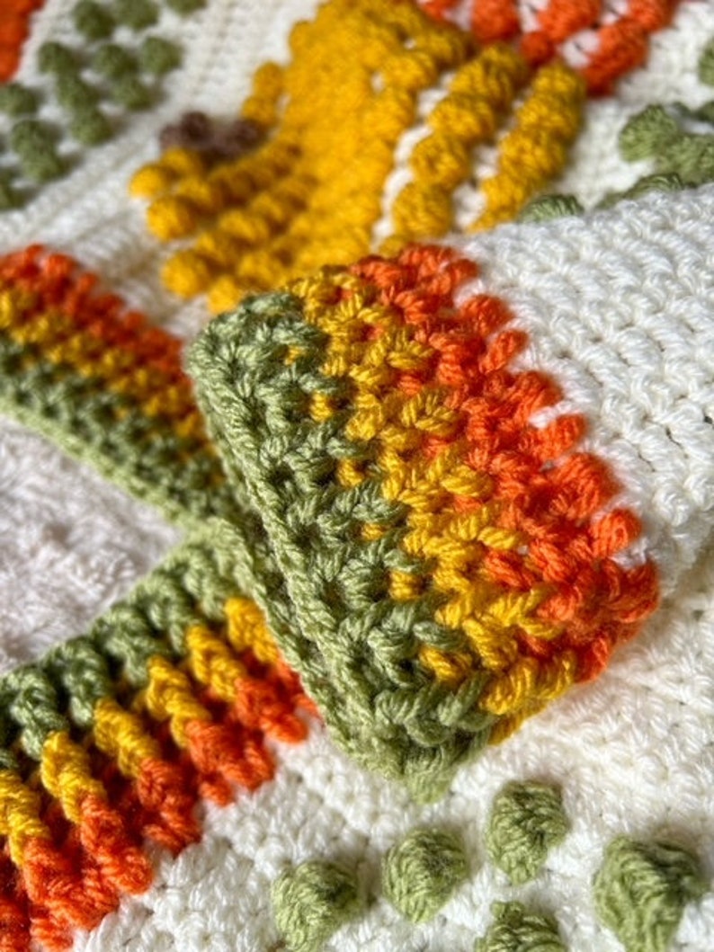May include: Close-up of a crocheted blanket with a colorful striped border. The blanket is made with white, green, yellow, and orange yarn.