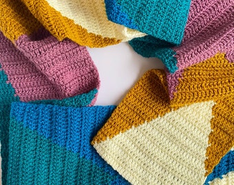 May include: A crocheted blanket with a geometric pattern in shades of teal, mustard yellow, cream, and dusty rose.