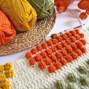 May include: A close-up of a crocheted blanket with a variety of colors and textures. The blanket features a pattern of orange, green, and yellow yarn. The blanket is being worked on with a crochet hook.