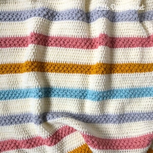 May include: A striped crochet blanket with a textured stitch pattern. The blanket is made in shades of white, grey, pink, blue, and yellow.