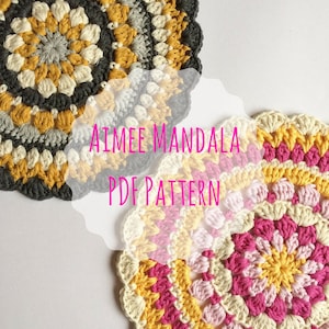 May include: Two crocheted mandalas, one in grey, yellow, and white, and the other in pink, yellow, and white. The text "Aimee Mandala PDF Pattern" is superimposed on the image.
