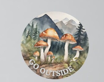 Könnte beinhalten: Eine Aquarell-Illustration von Pilzen, die in einem Wald mit Bergen im Hintergrund wachsen. Der Text "GO OUTSIDE" ist in einer Vintage-Schriftart geschrieben.