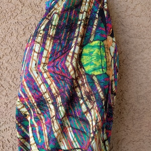 May include: A white fabric with a colorful abstract pattern. The pattern features shades of green, blue, purple, red, and yellow. The fabric is folded and draped over a surface.