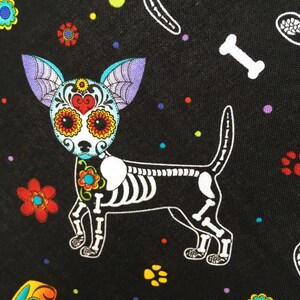 May include: A black fabric with a white skeletal chihuahua with colorful sugar skull details. The background is black with colorful polka dots and flowers.