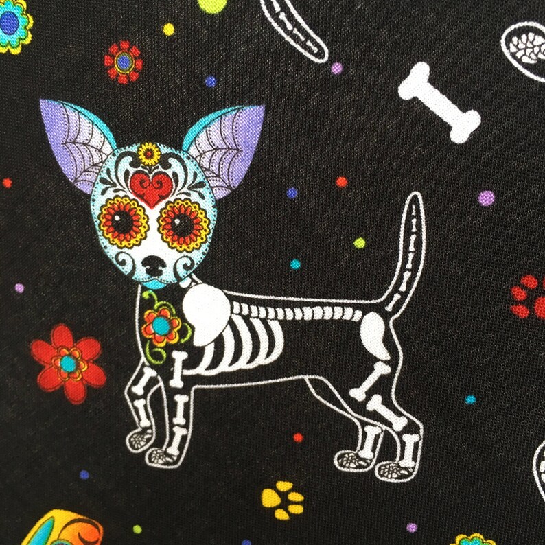 May include: A black fabric with a white skeletal chihuahua with colorful sugar skull details. The background is black with colorful polka dots and flowers.
