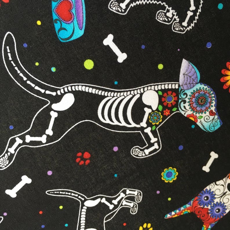 May include: Black fabric with a repeating pattern of white skeleton dogs with colorful floral details. The dogs are in a day of the dead style.