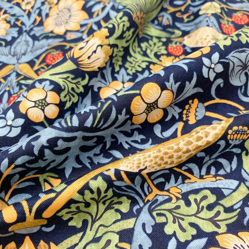 May include: Close-up of navy blue fabric with a floral pattern. The design features yellow flowers, green leaves, and light blue accents. A stylized lizard with yellow and brown markings is also visible.