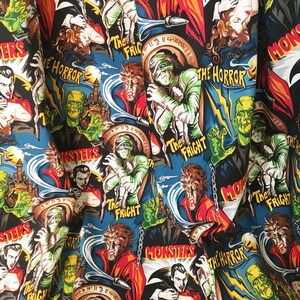 May include: A blue fabric with a repeating pattern of vintage movie posters featuring classic horror monsters. The posters feature images of Dracula, Frankenstein's monster, the Mummy, and the Wolfman. The text on the posters includes "Monsters", "The Horror", and "The Fright".