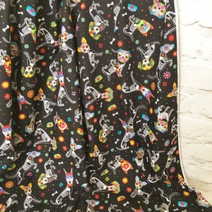 May include: Black fabric with a repeating pattern of white skeleton dogs with colorful flowers and bones. The dogs are in various poses, some are standing, some are sitting, and some are running.