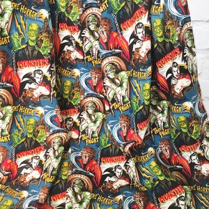 May include: A black and blue fabric with a repeating pattern of vintage horror movie posters featuring classic monsters like Dracula, Frankenstein, and the Mummy. The posters have text that reads "The Horror", "The Fright", and "Monsters".