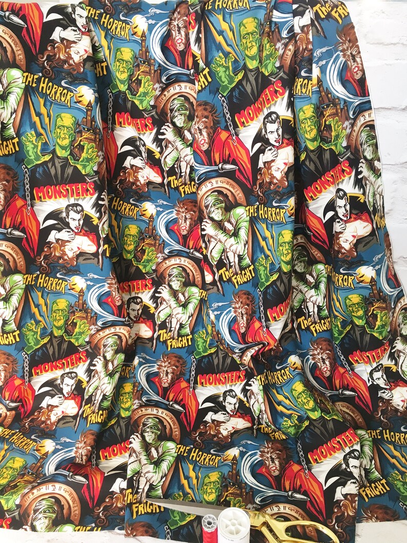 May include: A black and blue fabric with a repeating pattern of vintage horror movie posters featuring classic monsters like Dracula, Frankenstein, and the Mummy. The posters have text that reads "The Horror", "The Fright", and "Monsters".