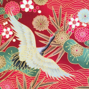 May include: A white crane with gold accents flies over a red background with gold and green floral patterns. The crane is in flight with its wings spread wide. The background is a repeating pattern of flowers, leaves, and swirls.