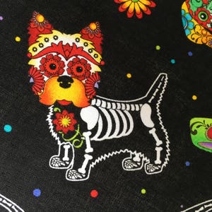 May include: A black fabric with a white skeletal dog with a colorful Day of the Dead sugar skull face. The dog is surrounded by colorful flowers and dots.