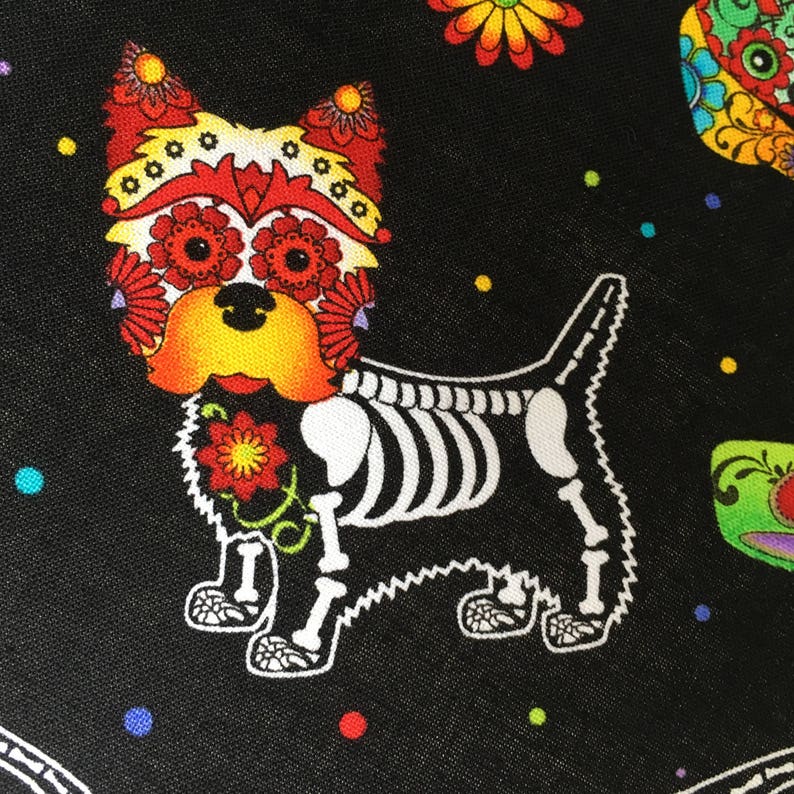 May include: A black fabric with a white skeletal dog with a colorful Day of the Dead sugar skull face. The dog is surrounded by colorful flowers and dots.