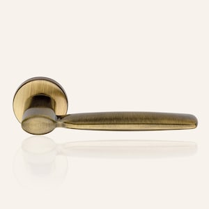 May include: A brushed brass door handle with a round base and a long, slightly curved lever.