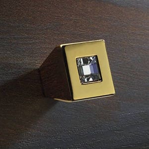 Könnte beinhalten: Ein goldener quadratischer Schrank-Knopf mit einem klaren Kristall in der Mitte.