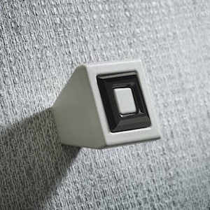 Könnte beinhalten: Ein weißer quadratischer Schrank-Knopf mit schwarzem Rand und einem weißen quadratischen Knopf in der Mitte.