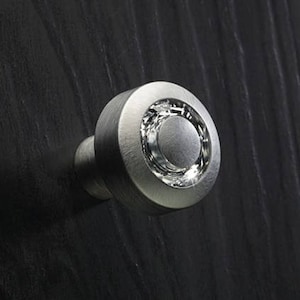 Könnte beinhalten: Ein silberner Schrank-Knopf mit einem runden, kristallartigen Design.