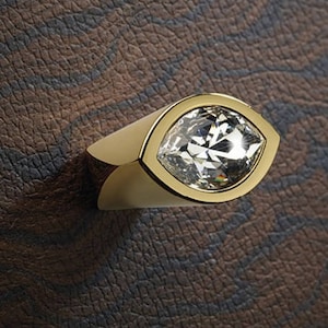 Könnte beinhalten: Goldfarbener Schrankknopf mit einem klaren Kristall in Form eines Auges.