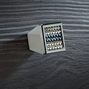 Könnte beinhalten: Ein silberner Schrankknopf mit einer quadratischen Fläche, die mit klaren und blauen Strasssteinen besetzt ist.