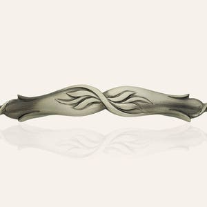 Könnte beinhalten: Ein silberfarbener Metall-Schrankgriff mit einem stilisierten floralen Design. Der Griff ist in Form von zwei ineinander verschlungenen Blättern mit einer gebürsteten Oberfläche.