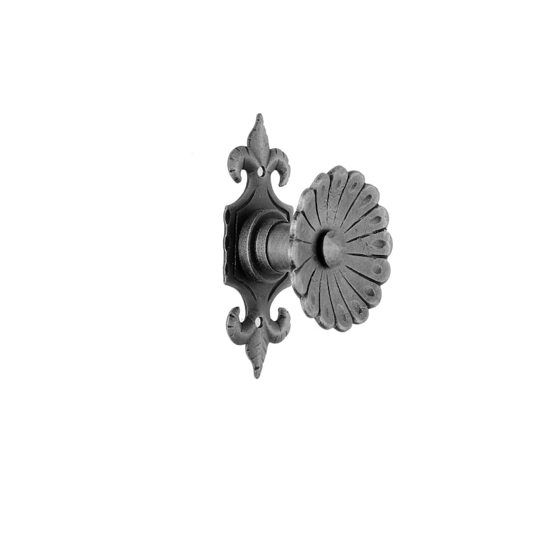 May include: A black metal door handle with a decorative floral design. The handle has a round knob with a fluted edge and a square backplate with a fleur-de-lis design.